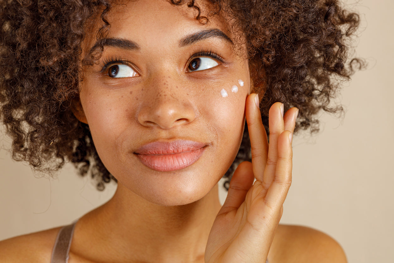 dark skin woman applying 3 dabs of moisturizer on skin