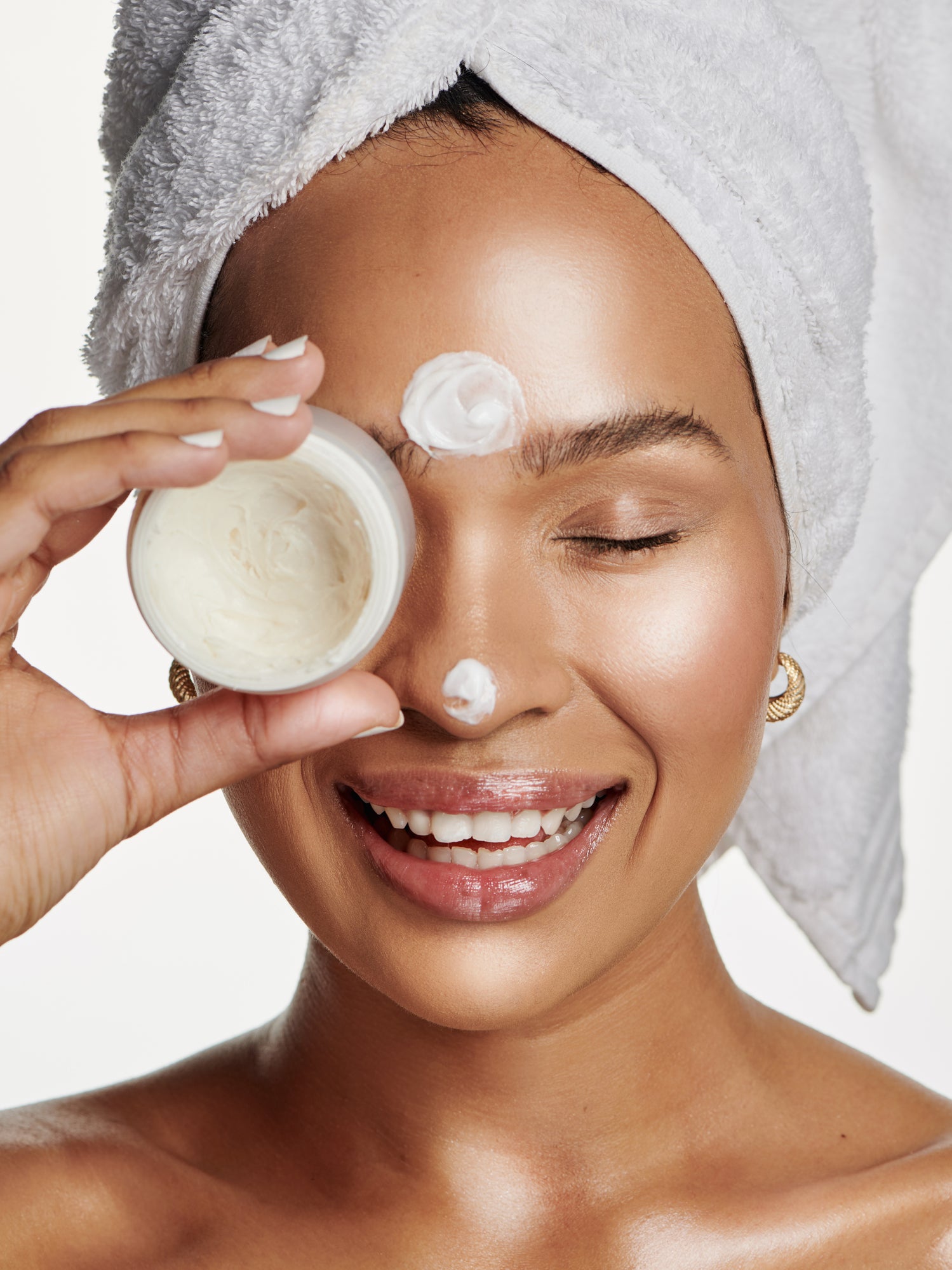 young beautiful black female applying face cream with bath towel wrapped around her head