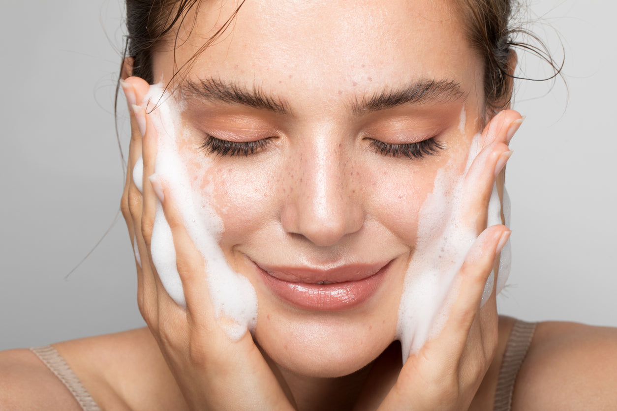 Young female model cleansing her face with Organic La Mousse Soothing Foam Cleanser with a white background